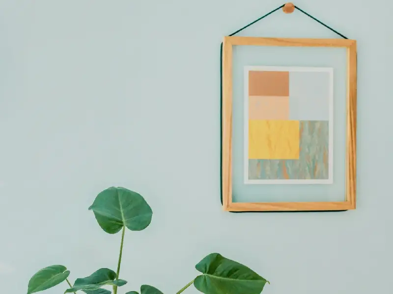 A picture frame hanging on the wall next to a plant.
