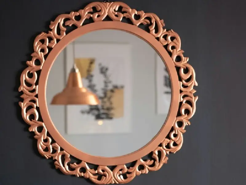A mirror with a gold frame and a lamp in the background.