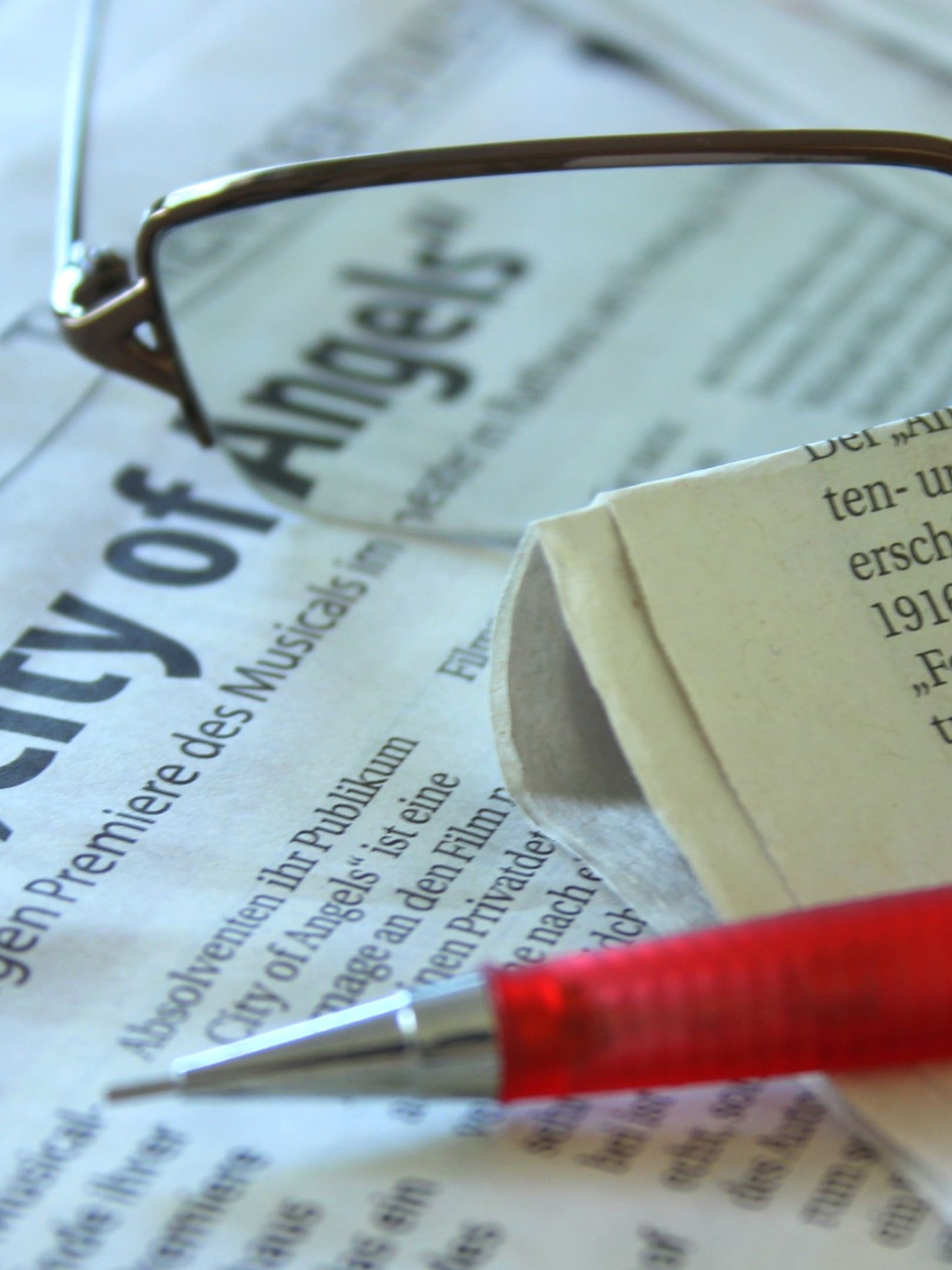 A pair of glasses and a pen on top of a newspaper.