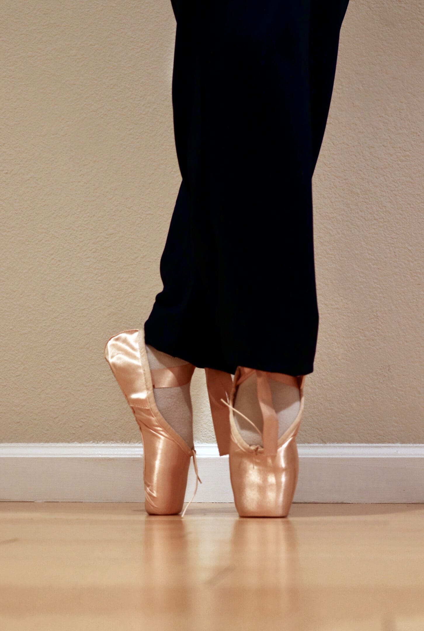 A person standing on the floor with their feet in pointe shoes.